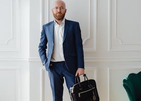 Bald businessman in blue suit holding a briefcase indoors.